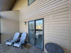 Spacious balcony with wood-finish flooring, featuring horizontal siding, dark-framed sliding glass doors, and an exterior wall lantern