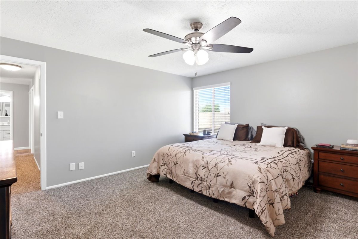 Bedroom featuring neutral gray wall paint, textured carpet flooring, and a ceiling fan with integrated lighting