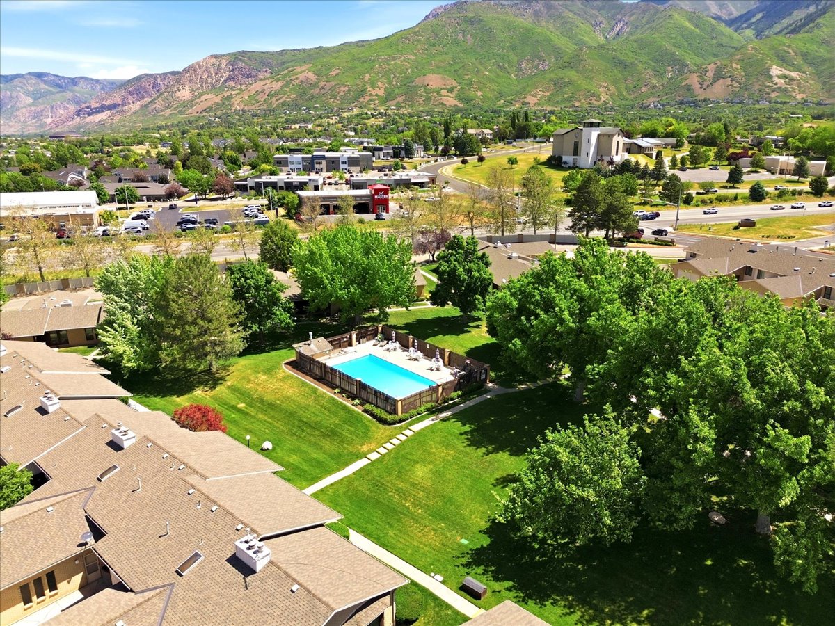 Outdoor swimming pool with surrounding patio, green lawn areas, mature trees, and mountain backdrop