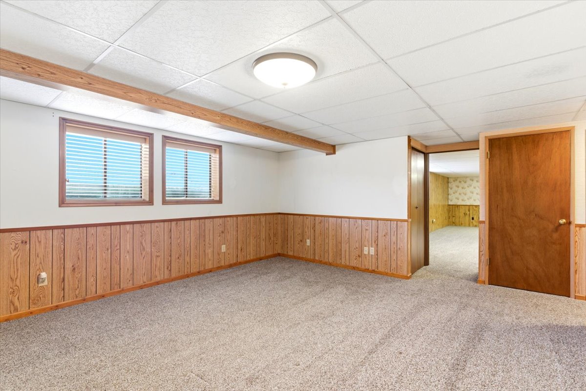 Spacious room featuring light wood-panel wainscoting, two windows with blinds, and neutral carpeting