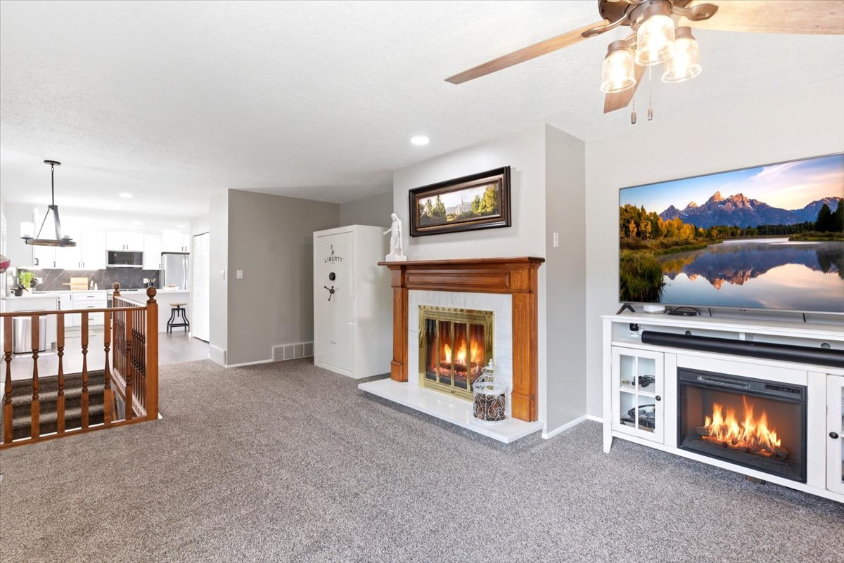 Living area featuring a traditional wood-mantel fireplace with a tiled surround, grey carpeting, and a ceiling fan with light fixture