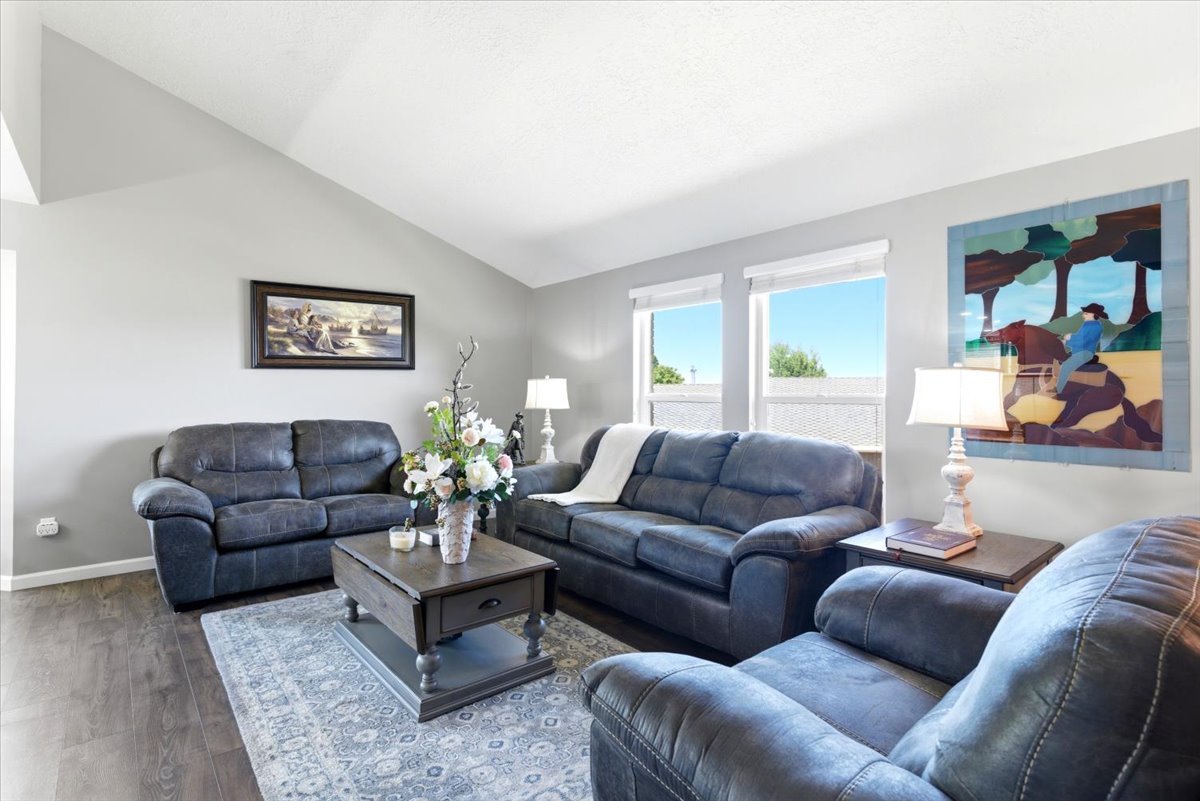 Vaulted ceiling living area featuring wood-finish flooring, light grey wall tones, and multiple windows