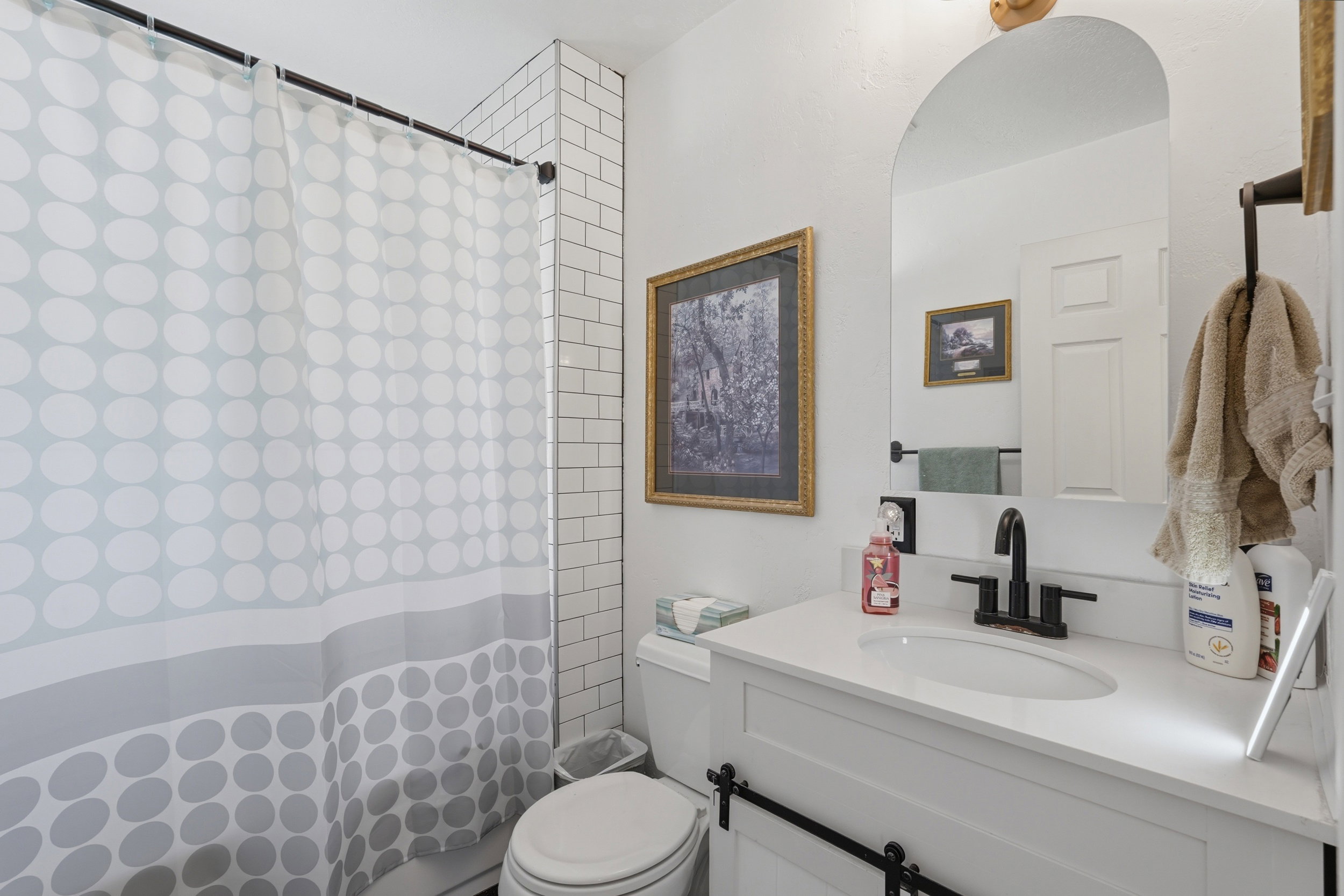 Bathroom featuring white subway tile surround, white vanity with integrated sink, black hardware, an arched mirror, and white walls