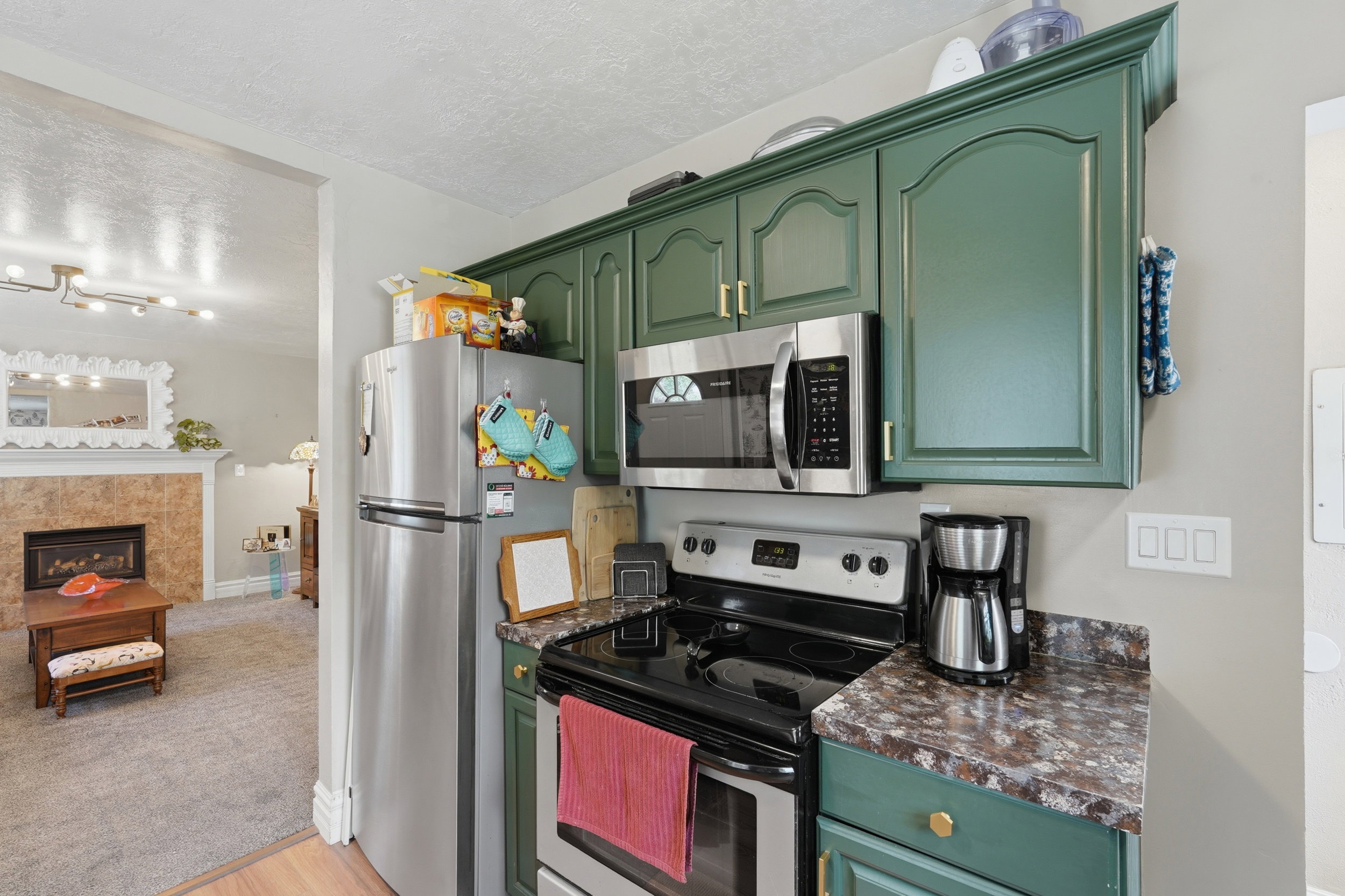 Kitchen area featuring green cabinetry with gold-tone hardware, a stainless steel refrigerator, and a stainless steel over-the-range microwave