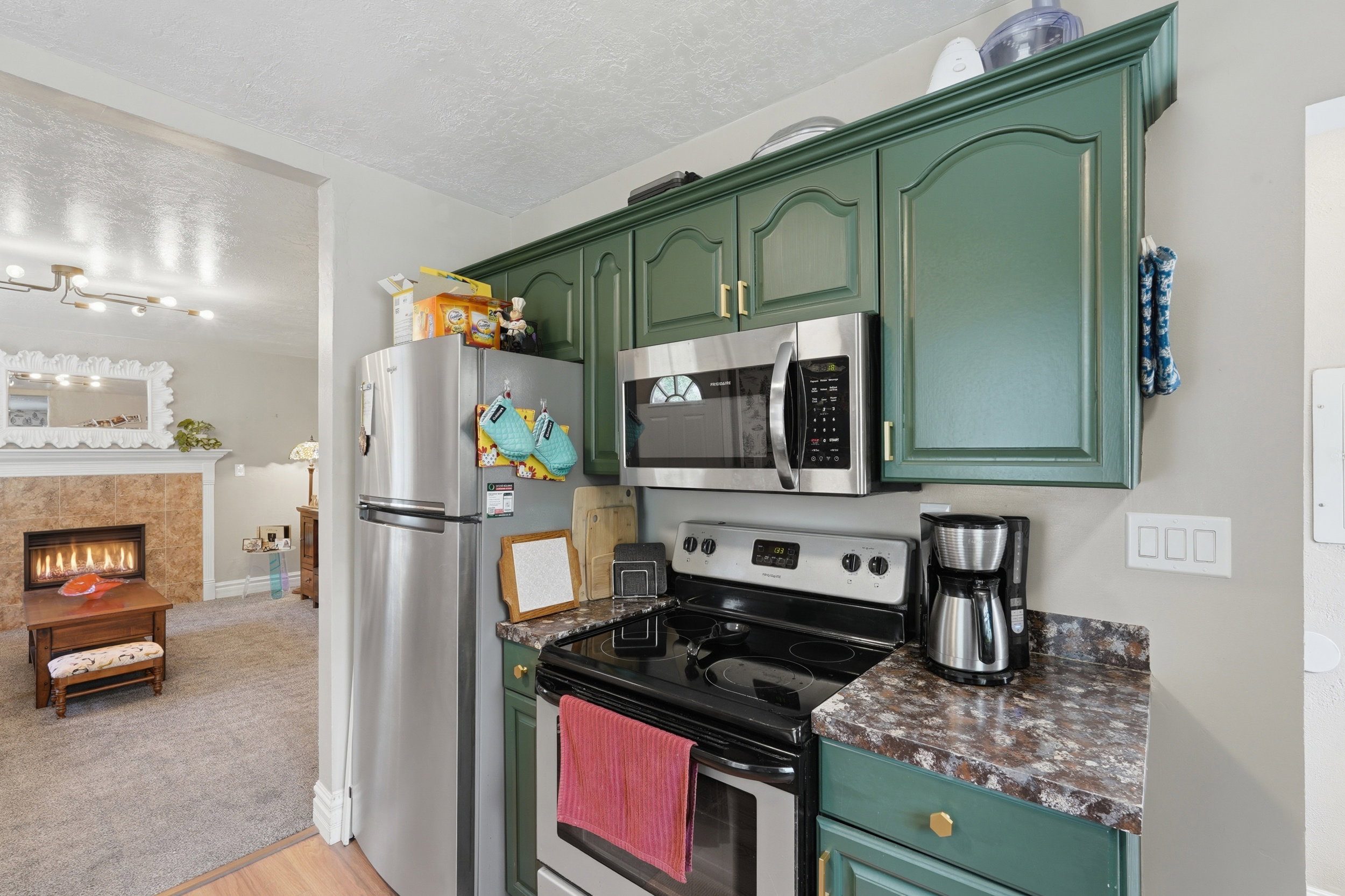 Kitchen featuring green cabinetry with gold-tone hardware, stainless steel appliances, and a dark speckled countertop