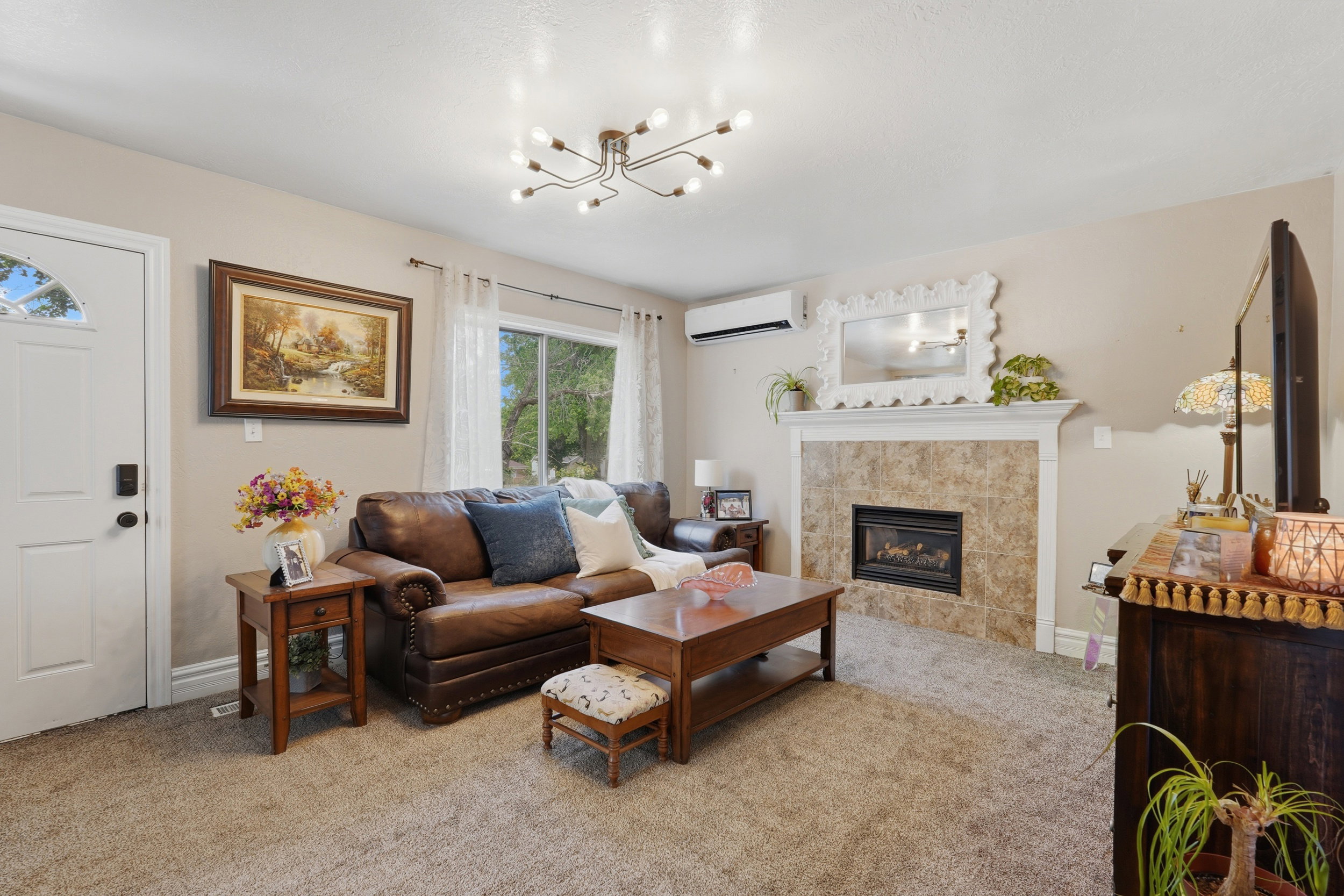 Living area featuring a gas fireplace with a tiled surround and white mantel, neutral carpeting, and a modern ceiling light fixture
