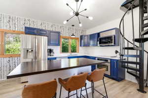 Modern kitchen with blue cabinetry, stainless steel appliances, a spacious island with a dark wood-finish countertop, and a white hexagonal tile backsplash