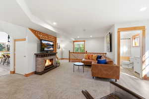 Carpeted living area featuring a stone-clad fireplace with a dark wood mantel, recessed lighting, wood-finish flooring, and natural wood trim accents