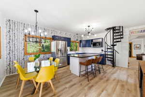 Open-concept living space with wood-finish flooring, a spiral staircase, and a kitchen featuring stainless steel appliances, blue cabinetry, and a black countertop island