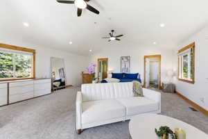 Spacious room featuring vaulted ceilings with two ceiling fans and recessed lighting, light-colored carpet flooring, and natural wood window and door trim