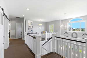 Upper-level landing featuring a white balustrade with dark wood-finish handrails, a large arched window, a spherical chandelier, recessed lighting, and a built-in bookcase
