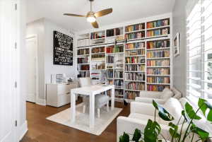Dedicated office space featuring extensive built-in shelving, a rolling library ladder, wood-finish flooring, and a ceiling fan