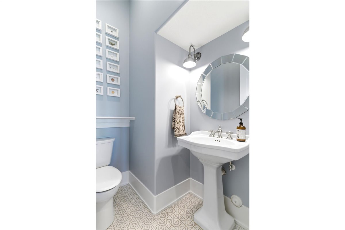 Pedestal sink with polished chrome fixtures, accented by a decorative round mirror
