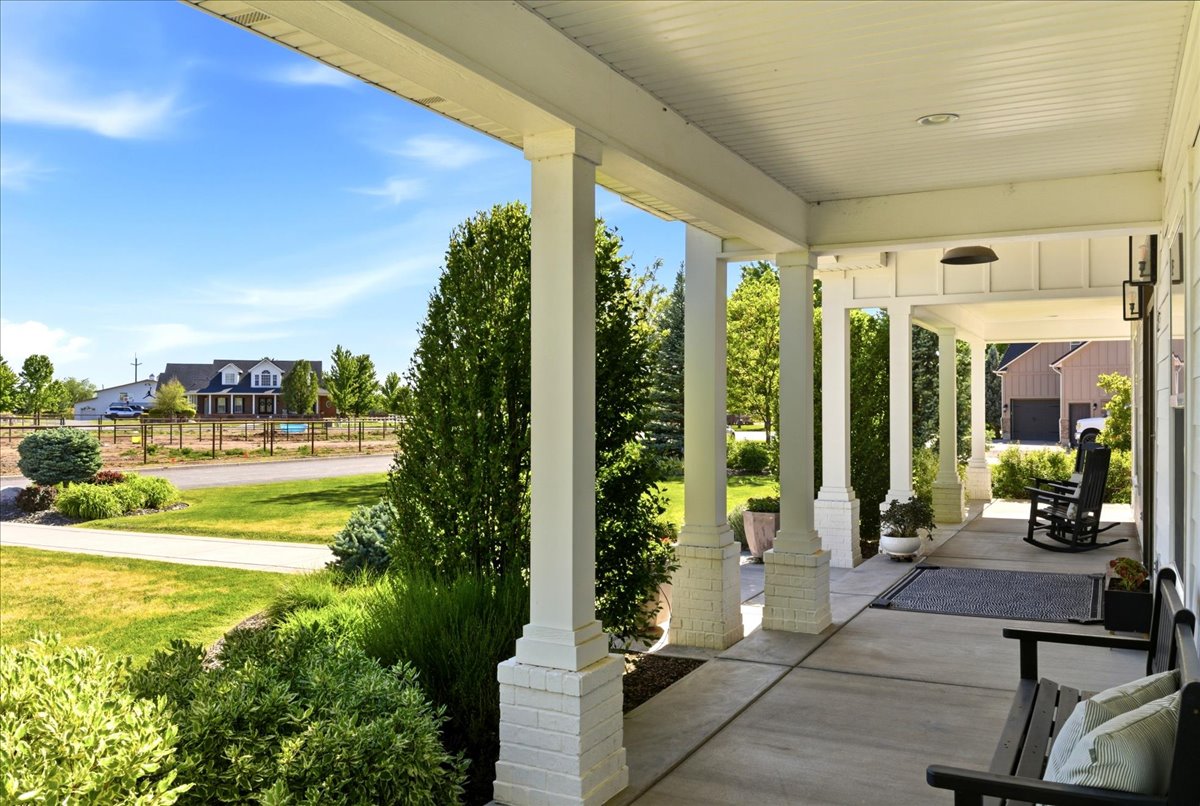 Expansive covered front porch featuring white columns with brick bases, planked ceiling, and a concrete surface