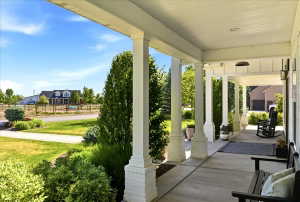 Expansive covered front porch featuring white columns with brick bases, planked ceiling, and a concrete surface