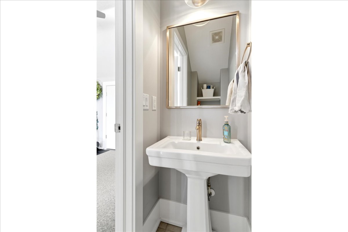 White pedestal sink with a gold-tone faucet, framed mirror, and light gray wall paint