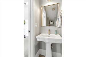 White pedestal sink with a gold-tone faucet, framed mirror, and light gray wall paint