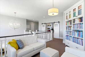 Open loft area featuring a contemporary drum pendant light, white baluster railings with black handrails, and built-in shelving with glass-front upper cabinets
