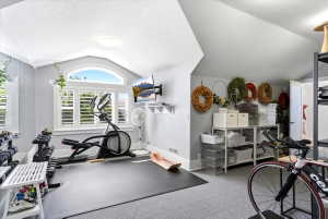 Vaulted ceiling featuring a large arched window with plantation shutters, light gray wall paneling, and a mounted flat-screen display