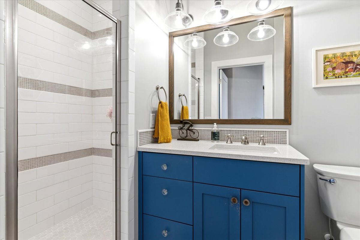 Bathroom featuring a glass-enclosed shower with white subway tile and decorative accent bands, a blue vanity with a white countertop and integrated sink, a framed mirror, and a wall-mounted light fixture