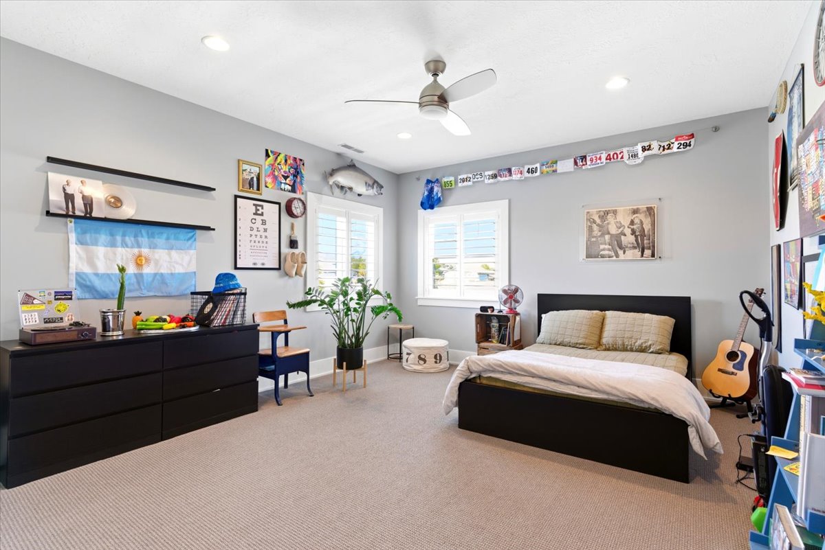 Spacious room featuring light gray walls, recessed lighting, a ceiling fan, plush carpet flooring, and two windows with white louvered shutters