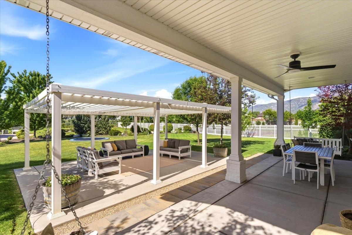 Expansive concrete patio featuring a covered portion with a ceiling fan and a separate pergola-covered section