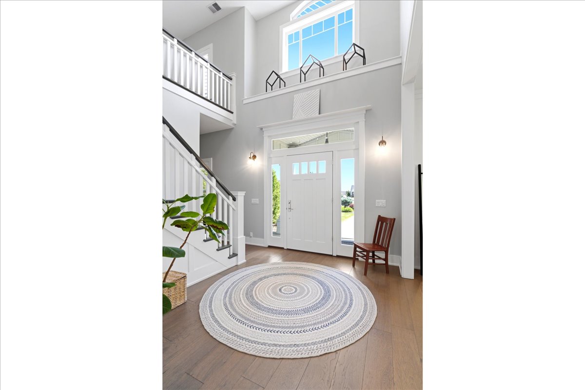 Two-story foyer featuring a prominent white staircase with dark handrails, wood-finish flooring, a transom window above the entry door, and a second-story window providing ample natural light