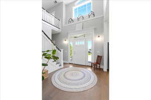 Two-story foyer featuring a prominent white staircase with dark handrails, wood-finish flooring, a transom window above the entry door, and a second-story window providing ample natural light