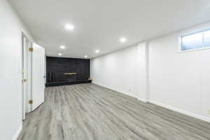 Spacious room featuring wood-finish flooring, recessed lighting, and a black brick fireplace with a hearth