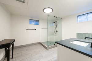 Contemporary bathroom featuring a frameless glass shower enclosure, dark matte fixtures, and a vanity with an integrated sink and dark countertop
