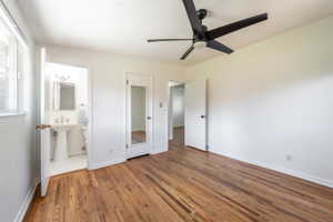 Spacious room featuring wood-finish flooring, white walls, and a modern ceiling fan and half bath attached