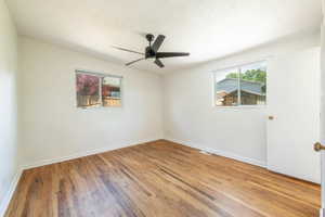 Room featuring wood-finish flooring, crisp white walls, and a contemporary black ceiling fan