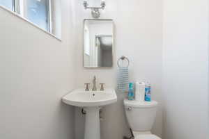 Pedestal sink with brushed nickel faucet, wall-mounted mirror, and overhead vanity light fixture