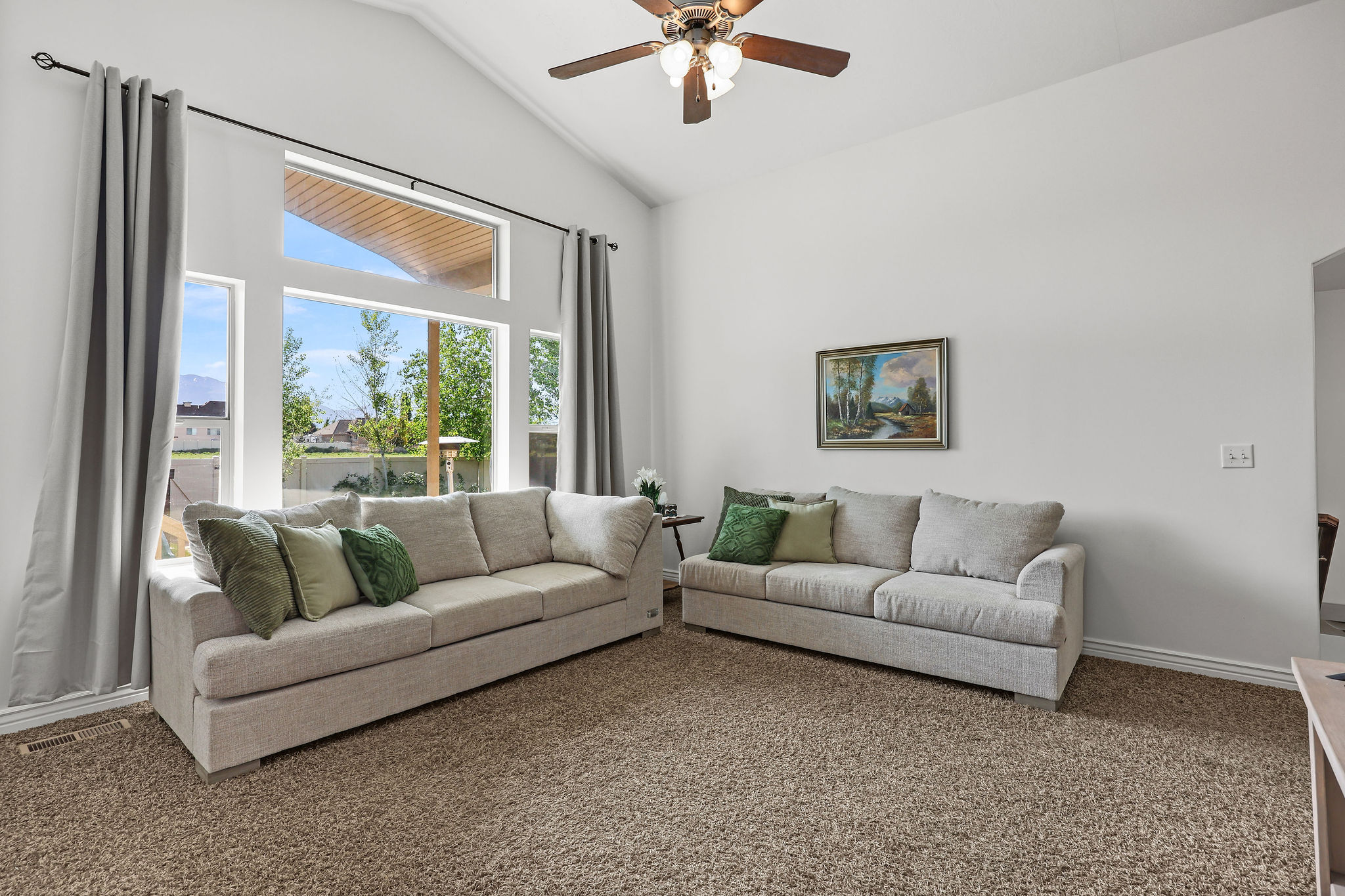Vaulted ceiling living area featuring a multi-pane window design, a ceiling fan with integrated lighting, and neutral carpet flooring