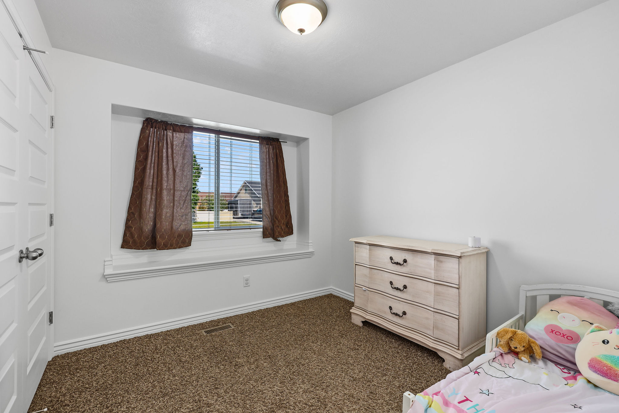 Room featuring neutral-toned walls, a single window with blinds and drapes, and an overhead flush-mount light fixture