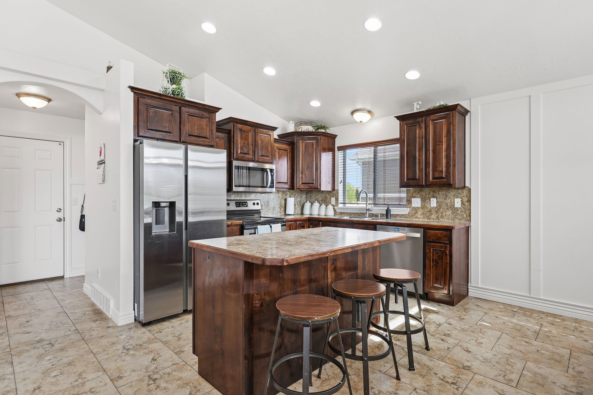 Kitchen featuring a breakfast bar island, wood-finish cabinetry, stainless steel appliances, tile flooring, and recessed lighting