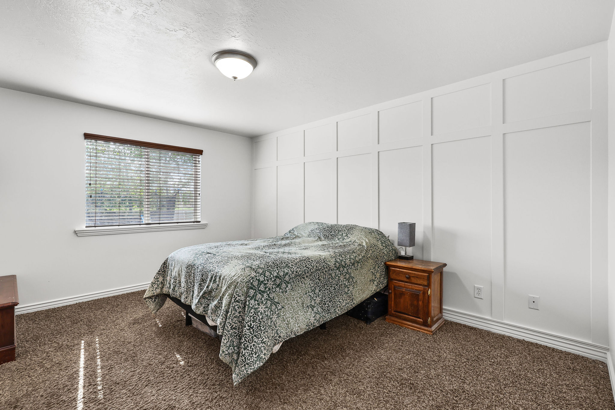 Bedroom featuring a decorative board and batten accent wall, neutral tone carpet, and a flush mount ceiling light fixture