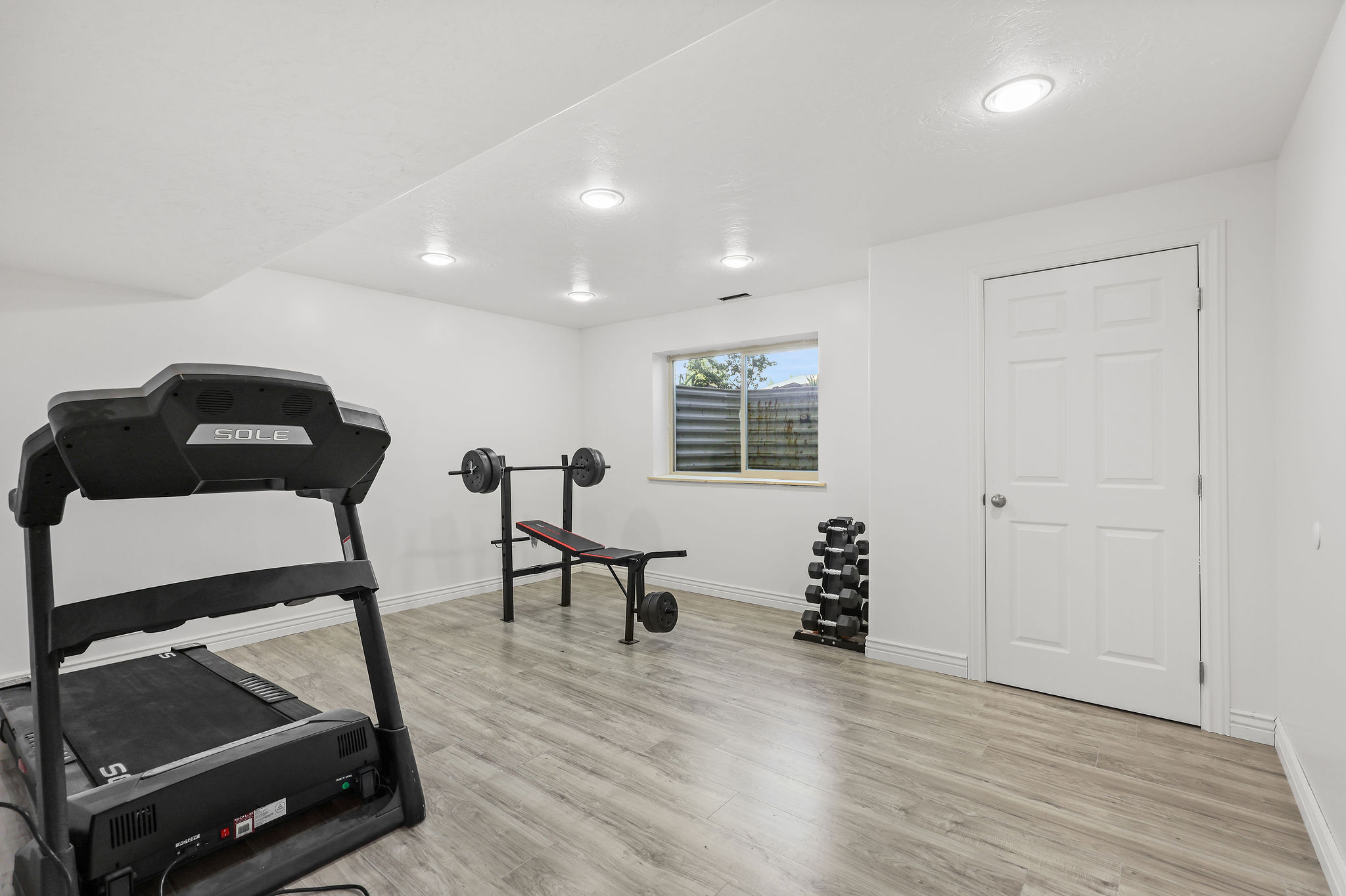 Spacious room featuring light wood-finish flooring, recessed lighting, and a white six-panel door