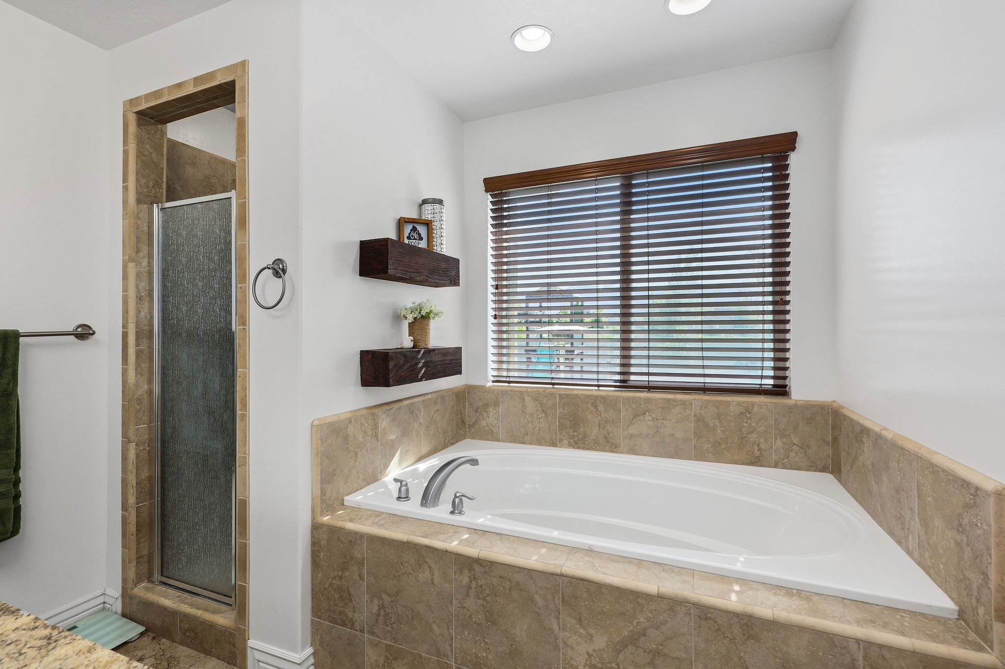 White drop-in tub with a tile surround, accompanied by a separate shower enclosure with a glass door