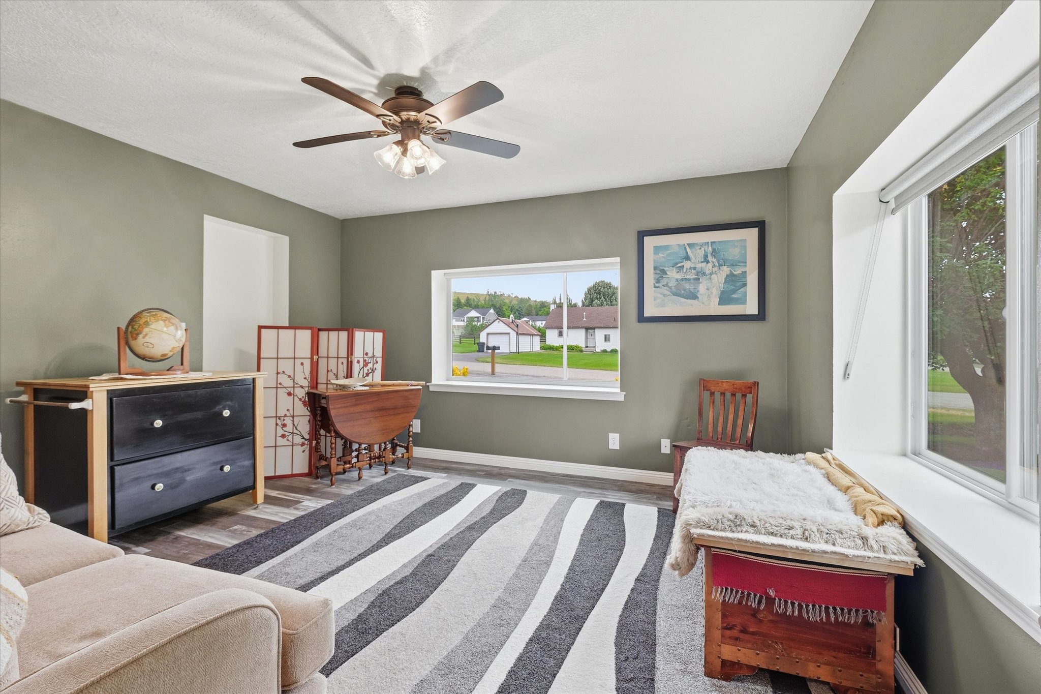 Spacious interior room featuring wood-finish flooring, two large windows, a ceiling fan with integrated lighting, and neutral wall tones