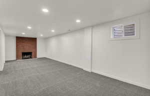 Spacious room featuring a brick fireplace, recessed lighting, and grey carpet flooring