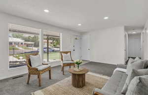 Bright living area featuring large windows with blinds, recessed lighting, and neutral carpet flooring