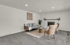 Spacious room featuring neutral carpeting, recessed lighting, and a white brick fireplace with a dark wood mantel