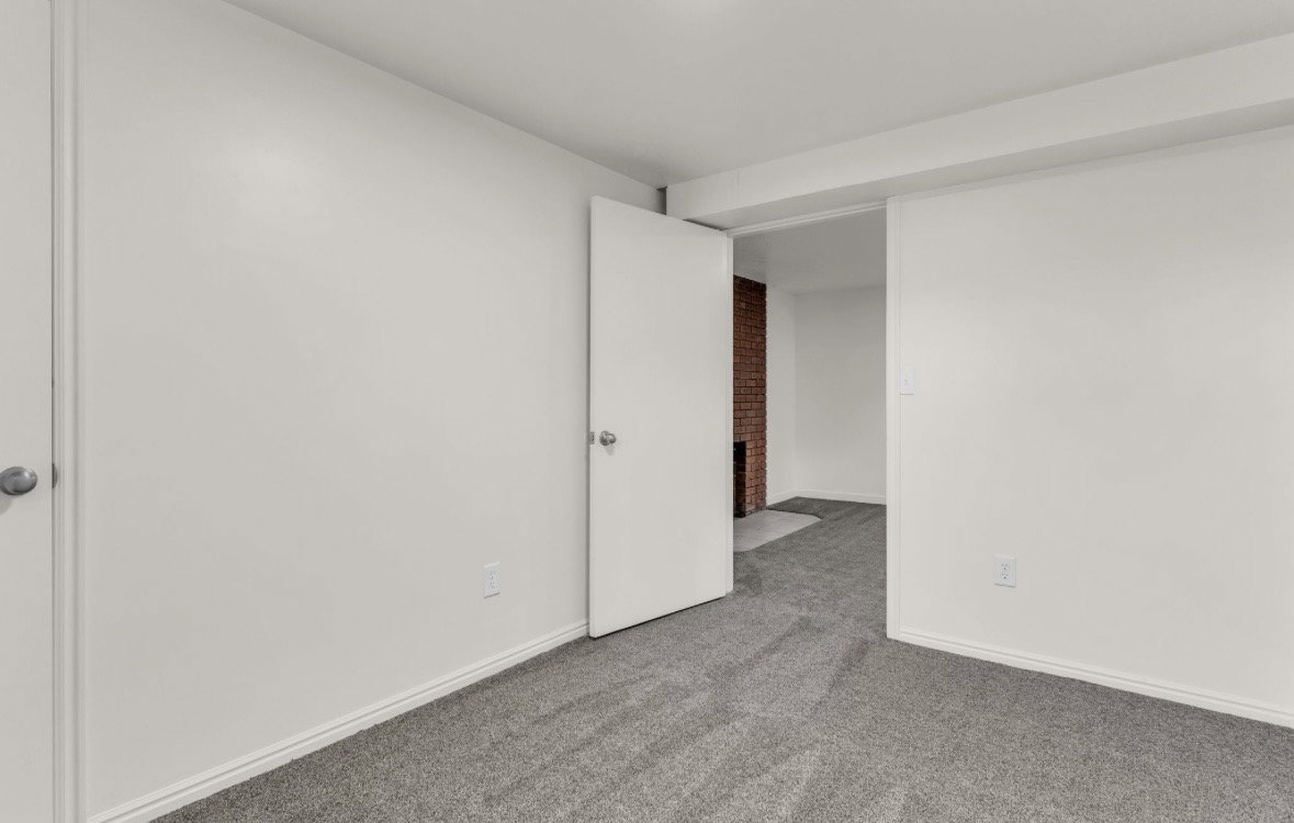Carpeted room featuring white walls, white trim, and a prominent doorway leading to an additional space with a visible red brick wall