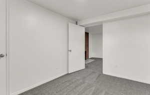 Carpeted room featuring white walls, white trim, and a prominent doorway leading to an additional space with a visible red brick wall