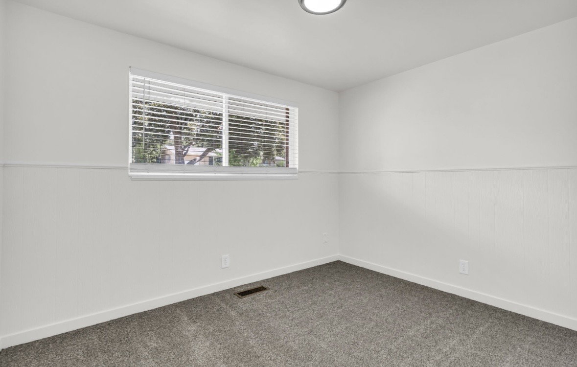 Room featuring a large window with blinds, paneling, neutral carpet, and a ceiling-mounted light fixture