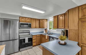 Kitchen featuring light wood cabinetry, light blue countertops, tile flooring, stainless steel appliances, and a window above the sink