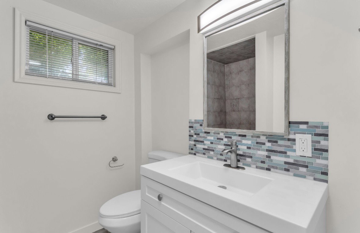 Bathroom featuring a white vanity with integrated sink, brushed nickel faucet, and a multi-tone tile backsplash
