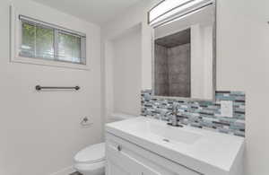 Bathroom featuring a white vanity with integrated sink, brushed nickel faucet, and a multi-tone tile backsplash