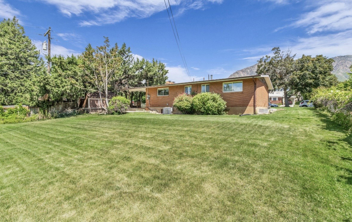 Expansive grassy yard area with mature perimeter trees and a brick-sided residence